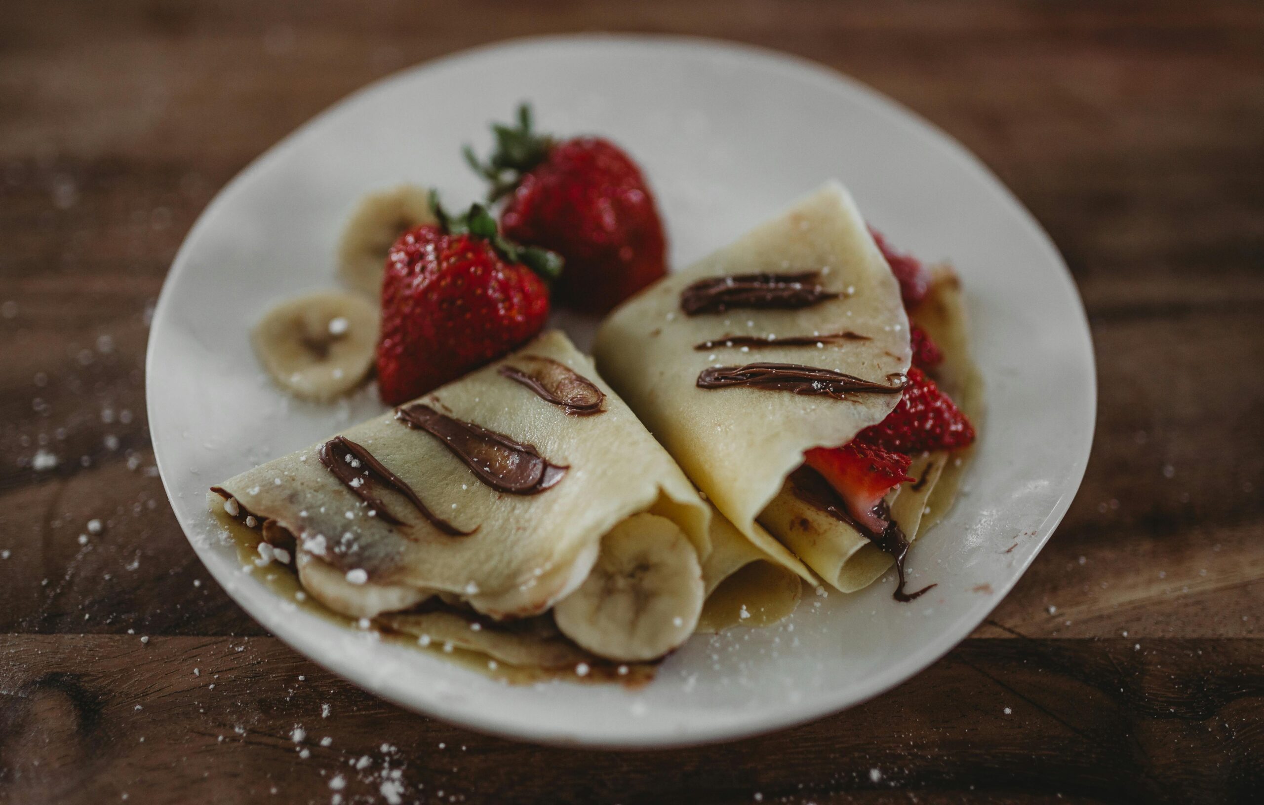 Tasty French crepes topped with fresh strawberries, bananas, and Nutella sauce.